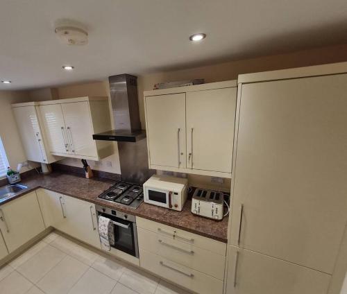 a kitchen with white cabinets and a stove and a microwave at Spacious 3-Bed House - Sleeps 8 Garden & Parking in Peterborough