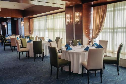 a dining room with white tables and chairs andwindows at Qafqaz Baku City Hotel & Residences in Baku