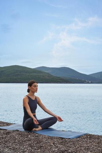 a woman sitting in a yoga pose by the water at The Chedi Luštica Bay in Tivat