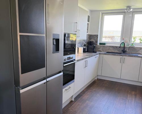 a kitchen with white cabinets and black appliances at Milton of Tullypowrie Cottage in Pitlochry