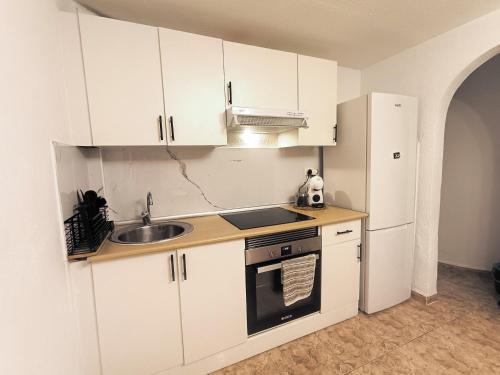 a kitchen with white cabinets and a sink and a refrigerator at Bellavista Basement in Costa Del Silencio