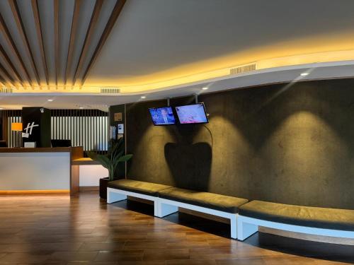 a lobby with a bench with two monitors on the wall at Holiday Inn Naples by IHG in Naples