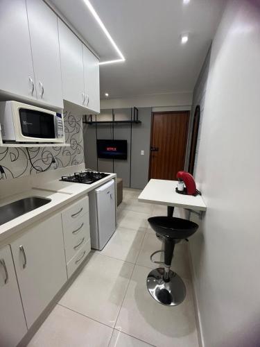 cocina con armarios blancos, mesa y taburete en Brasília Kit Sudoeste, en Brasilia