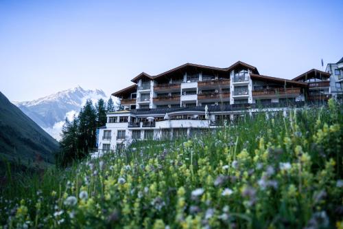 a building on a hill with a field of flowers at Hotel Bellevue - 4 Sterne superior in Obergurgl