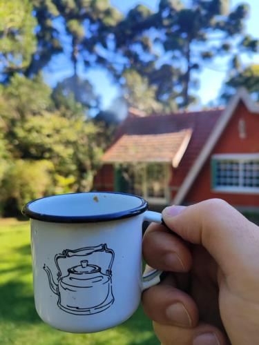 eine Hand hält eine Kaffeetasse vor einem Haus in der Unterkunft Chalé São Rafael - Recanto da Natureza in Gramado