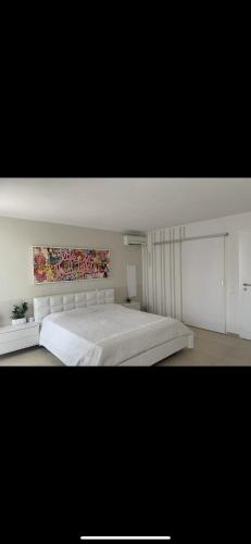 a bedroom with a large white bed with a painting on the wall at Affitta camere Locarno in Minusio