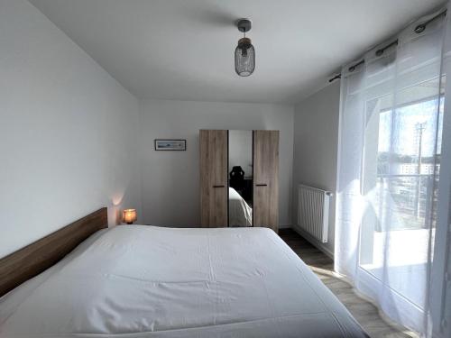 Un dormitorio con una gran cama blanca con ventana. en Le 30 - Vannes station - 4 pers parking, en Damgan