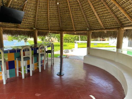 a patio with a table and chairs under a straw roof at Finca El Quijote con alberca y 6 cuartos in Atlixco