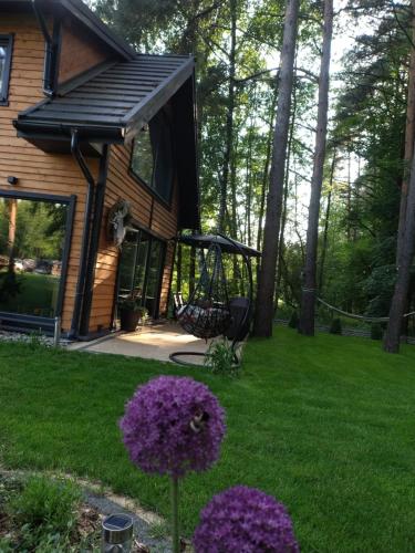 a house with a swing and purple flowers in the yard at Domek pod sosnami in Ełk