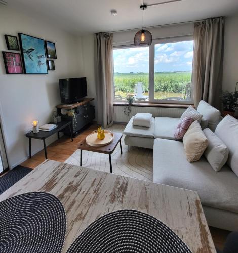 a living room with a white couch and a large window at Appartement 1 met uitzicht op de waterkant van Op de Roemte in Baflo