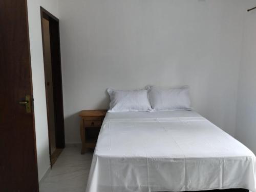 un lit avec des draps blancs et des oreillers dans une chambre dans l'établissement Casa em Paraty Portão Vermelho, à Parati