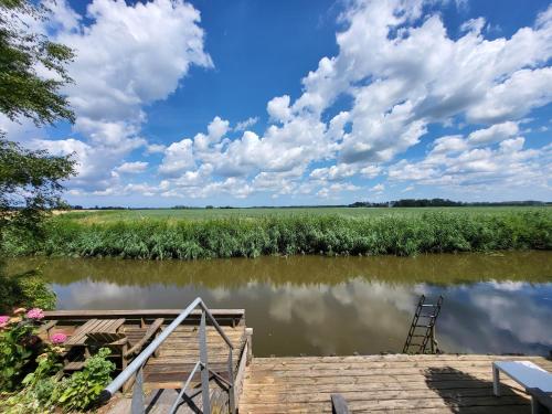 a dock on a river with a cloudy sky at Appartement 1 met uitzicht op de waterkant van Op de Roemte in Baflo