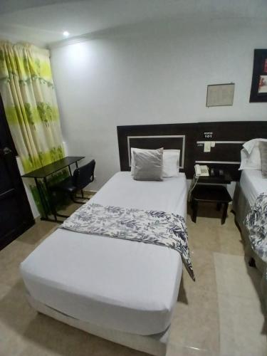 a bedroom with a white bed and a desk and a table at Hotel Plaza Norte Cali in Cali