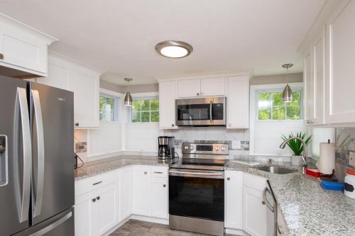 a kitchen with white cabinets and a stainless steel refrigerator at Cape Cod Cottage by Leavetown Vacations in Dennis Port