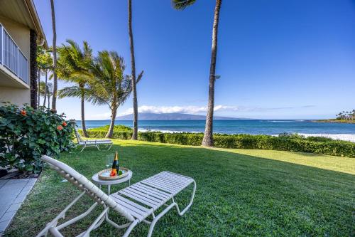 a lawn with a chair and a table with a bottle of wine at Napili Shores - Ocean Front Ground Floor in Kahana