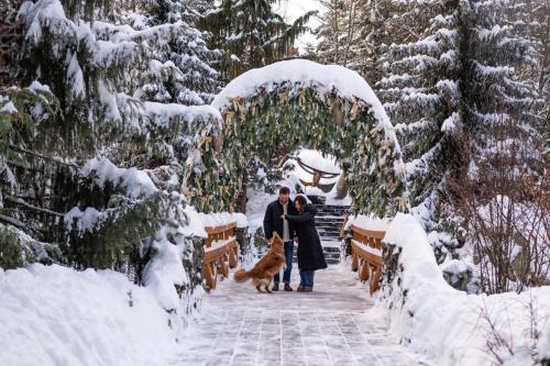 a couple and their dog walking under an arch in the snow at Four Seasons Resort Whistler in Whistler