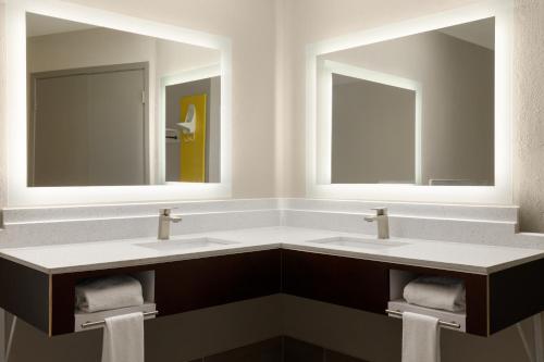 two sinks in a bathroom with two mirrors at Days Inn by Wyndham Suites Fredericksburg in Fredericksburg