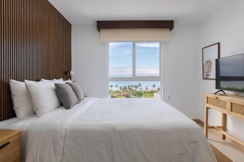 a white bedroom with a large bed and a television at Viva Jaco in Jacó