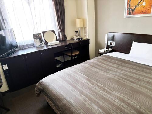 a hotel room with a bed and a desk with a mirror at Hotel Route-Inn Shibukawa in Shibukawa