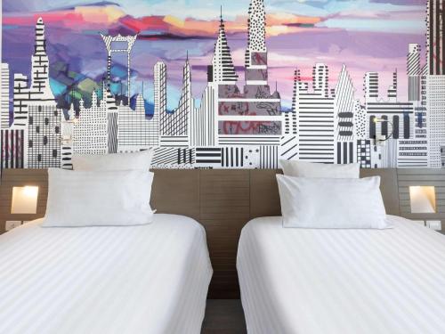 two beds in a room with a mural of a city at Novotel Bangkok on Siam Square in Bangkok