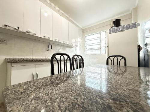 a kitchen with a marble counter top and black chairs at Pé na Areia Praia da Tupi II in Samaritá