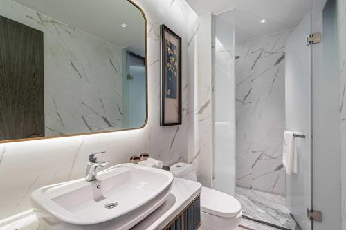 a white bathroom with a sink and a mirror at Grand Madison Wuhan Hankou on the Bund in Wuhan