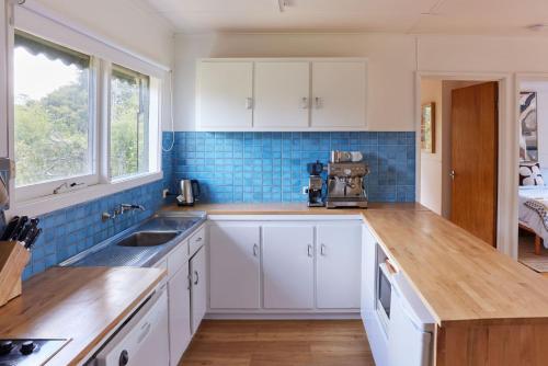una cocina con armarios blancos y azulejos azules en Lohr Ave Holiday Home, en Inverloch