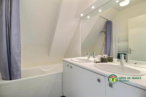 een badkamer met 2 wastafels, een bad en een spiegel bij La vigerie in Carnac