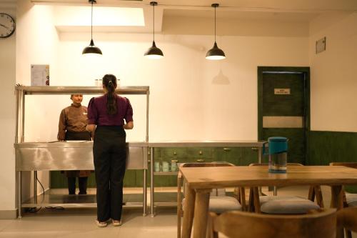 a woman standing in a room with two men in the background at Grihum Living Girls - FEMALE ONLY in Rānchī