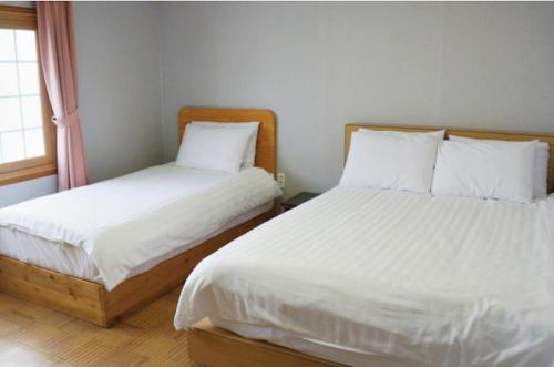 a bedroom with two beds with white sheets and a window at Hotel G in Jeju