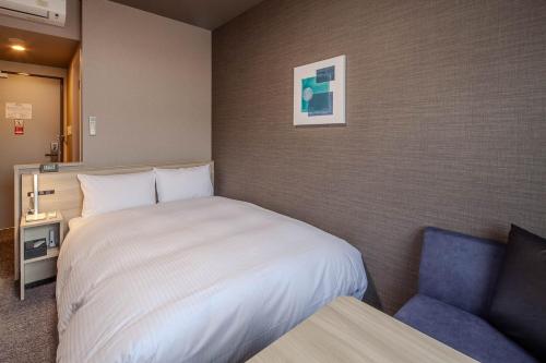a bedroom with a white bed and a blue chair at Hotel Route Inn Kanegasaki 
