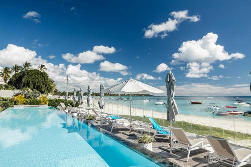 a swimming pool with chairs and umbrellas and the ocean at OBiches Penthouse C1 Beachfront Complex in Trou aux Biches