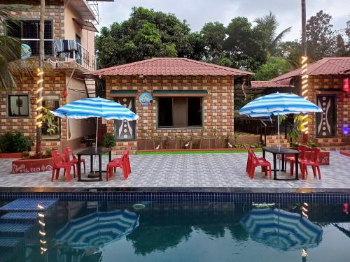 two tables and chairs with umbrellas next to a pool at Daksh Holiday Home in Alibaug