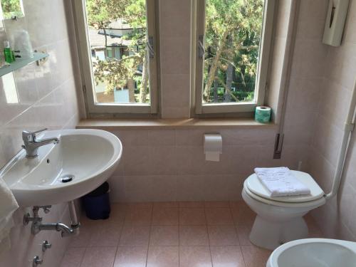 a bathroom with a sink and a toilet and two windows at Pensione Giardino in Lignano Sabbiadoro