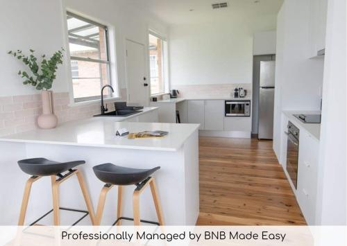a kitchen with a white counter and two stools at Haven on Hill - Modern & Charming, Touch of Pink in Orange