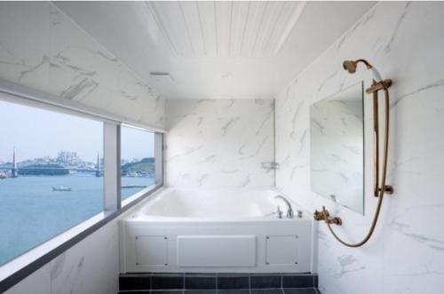 a white bathroom with a tub and a window at Blanc Hotel & Resort in Yeosu