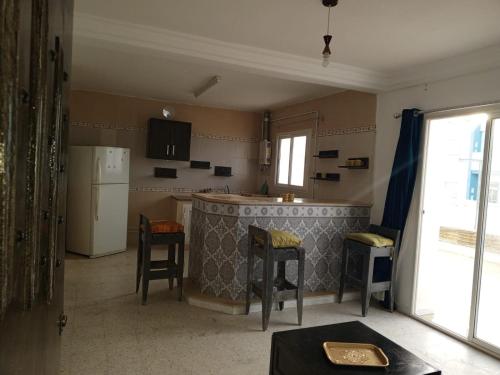 a kitchen with a bar with stools and a refrigerator at Résidence BAYA in Chott Meriem