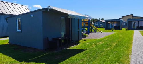 a blue tiny house with a playground in a yard at Audronašų Vilų Nameliai in Šventoji