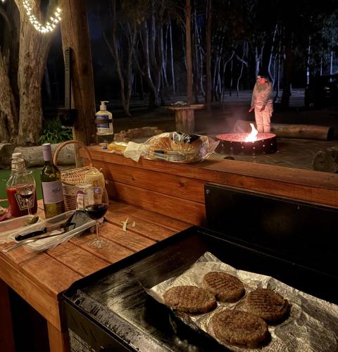 a table with a grill with hamburgers and a fire at Tiny Homes Escape at Grampians Edge by Tiny Away in Dadswells Bridge