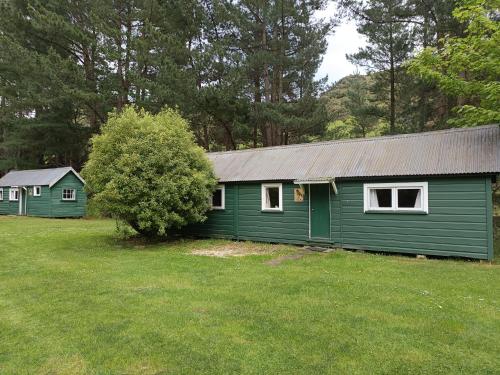 a green building with a tree in a yard at Danseys Pass Holiday Park in Oamaru