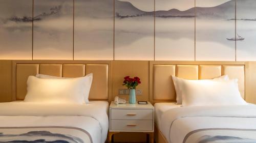 two beds in a hotel room with a vase of flowers at Weilai J Hotel Kunming New Luoshuiwan Branch in Kunming
