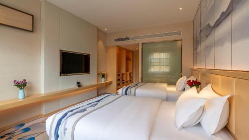 two beds in a hotel room with a television at Weilai J Hotel Kunming New Luoshuiwan Branch in Kunming