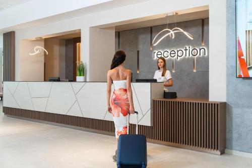 a woman with a suitcase standing in front of a reception at Festa Panorama Hotel in Nesebar