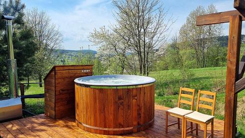 a wooden hot tub on a deck with two chairs at Domki Na Wzgórzu in Nowica