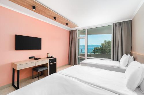 a hotel room with two beds and a desk and a window at Festa Panorama Hotel in Nesebar