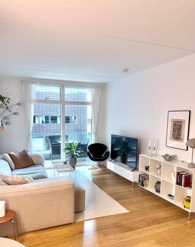a white living room with a couch and a tv at Heart of Aarhus, modern apartment and paid parking nearby in Aarhus