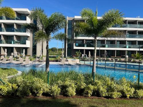 a swimming pool with chairs and palm trees in front of a building at FLAT BEACH CLASS SUMMEr PORTO DE GALINHAS in Porto De Galinhas