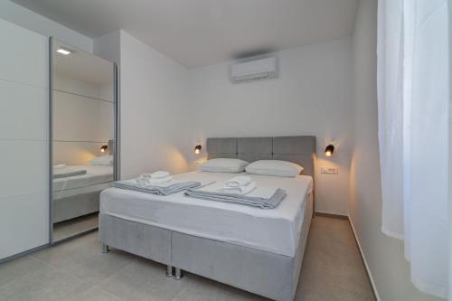 a white bedroom with a bed and a mirror at Apartmani Olimp2 in Sveti Juraj
