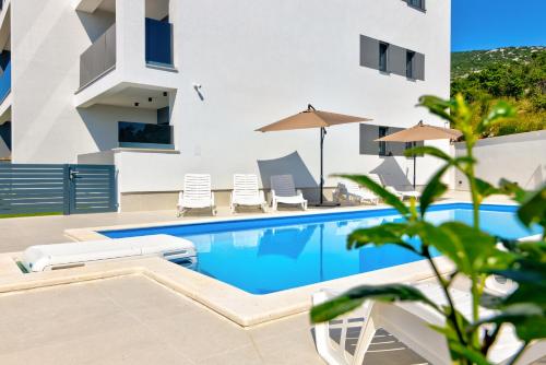 a swimming pool with chairs and umbrellas next to a building at Apartmani Olimp2 in Sveti Juraj