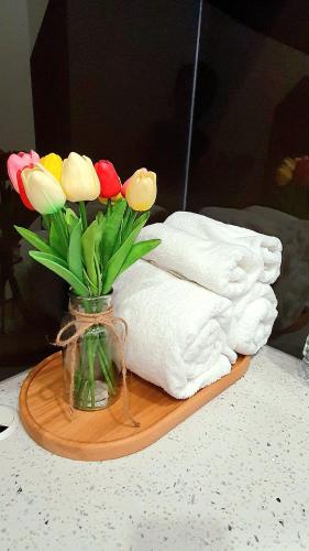 a vase of flowers on a table with a towel at Andi Homestay-Vinhomes Grand Park in Gò Công
